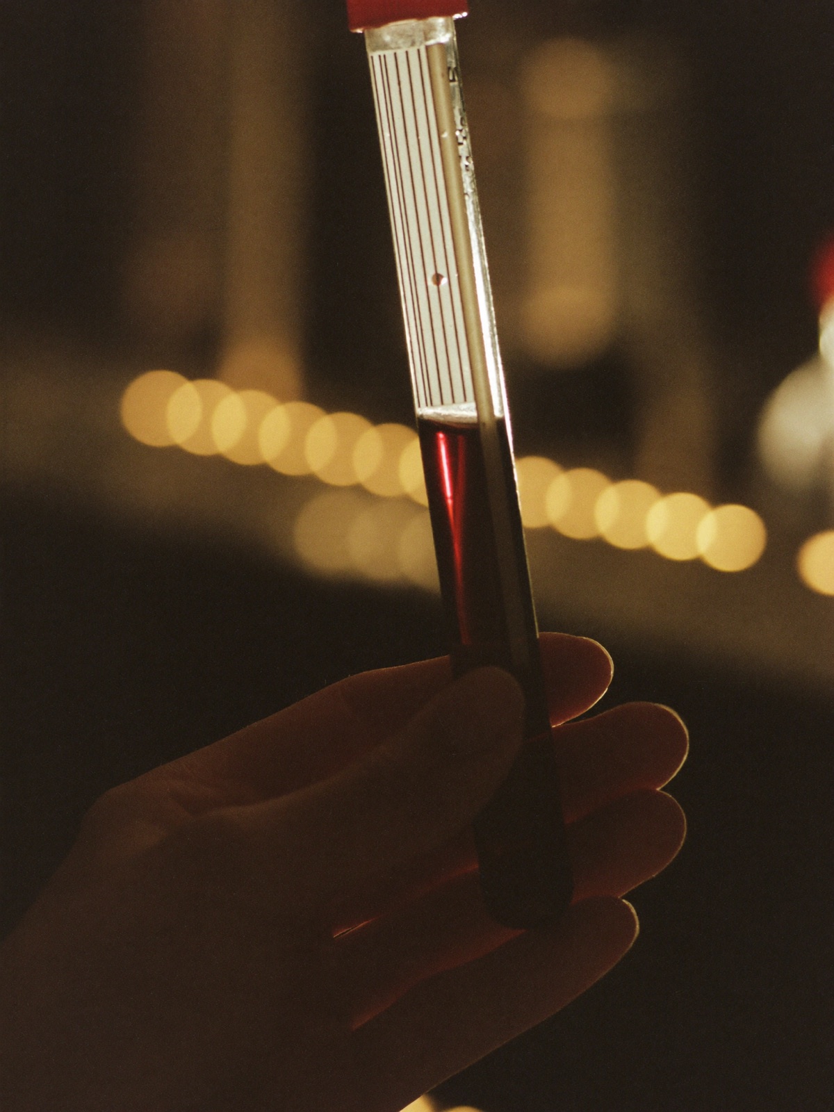 A hand holding a glass test tube of deep amber liquid against warm golden bokeh light