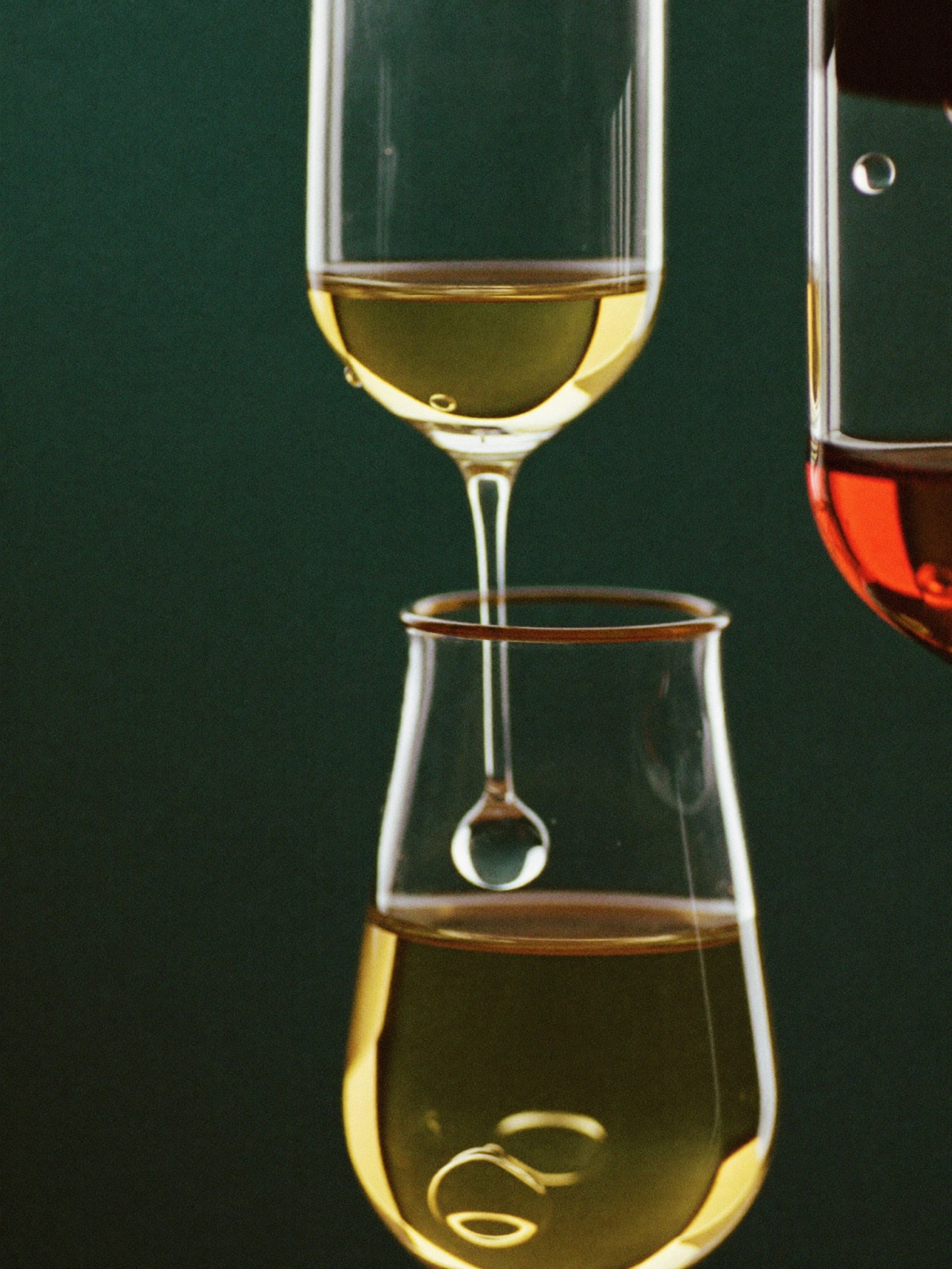 Glass vessels holding golden liquid catching warm light against a deep green background
