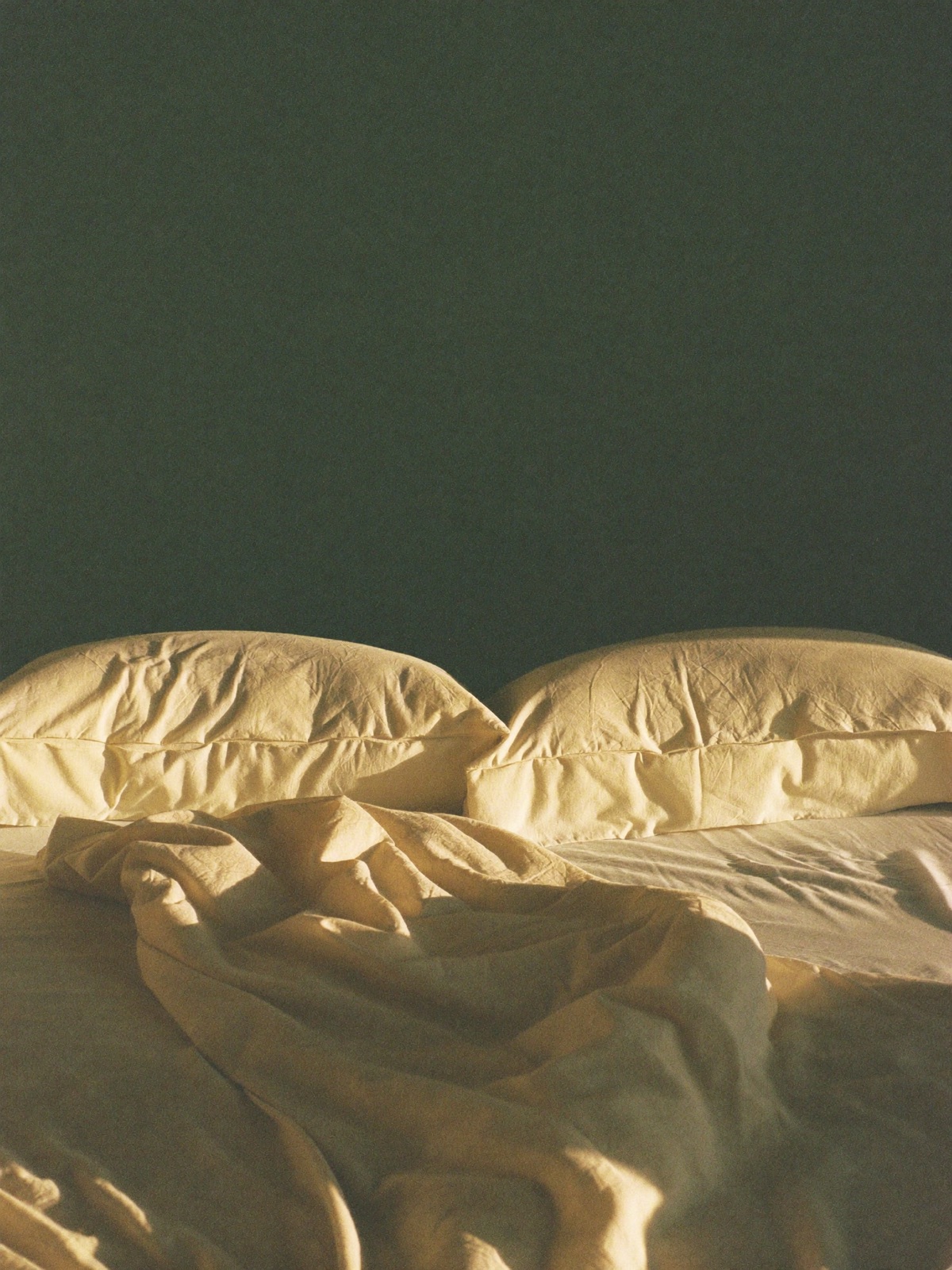 Ivory linen bedding at dawn with low golden light against a deep sage wall